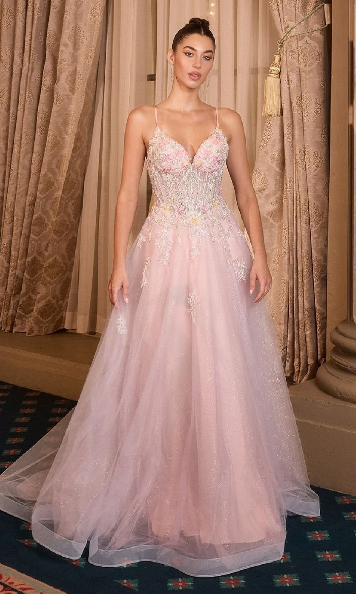 A woman stands indoors in front of beige curtains wearing the Classic Long Pink Prom Dress: Andrea and Leo A1477, featuring an A-line silhouette, embroidered flowers, a fitted bodice, and corset back details.